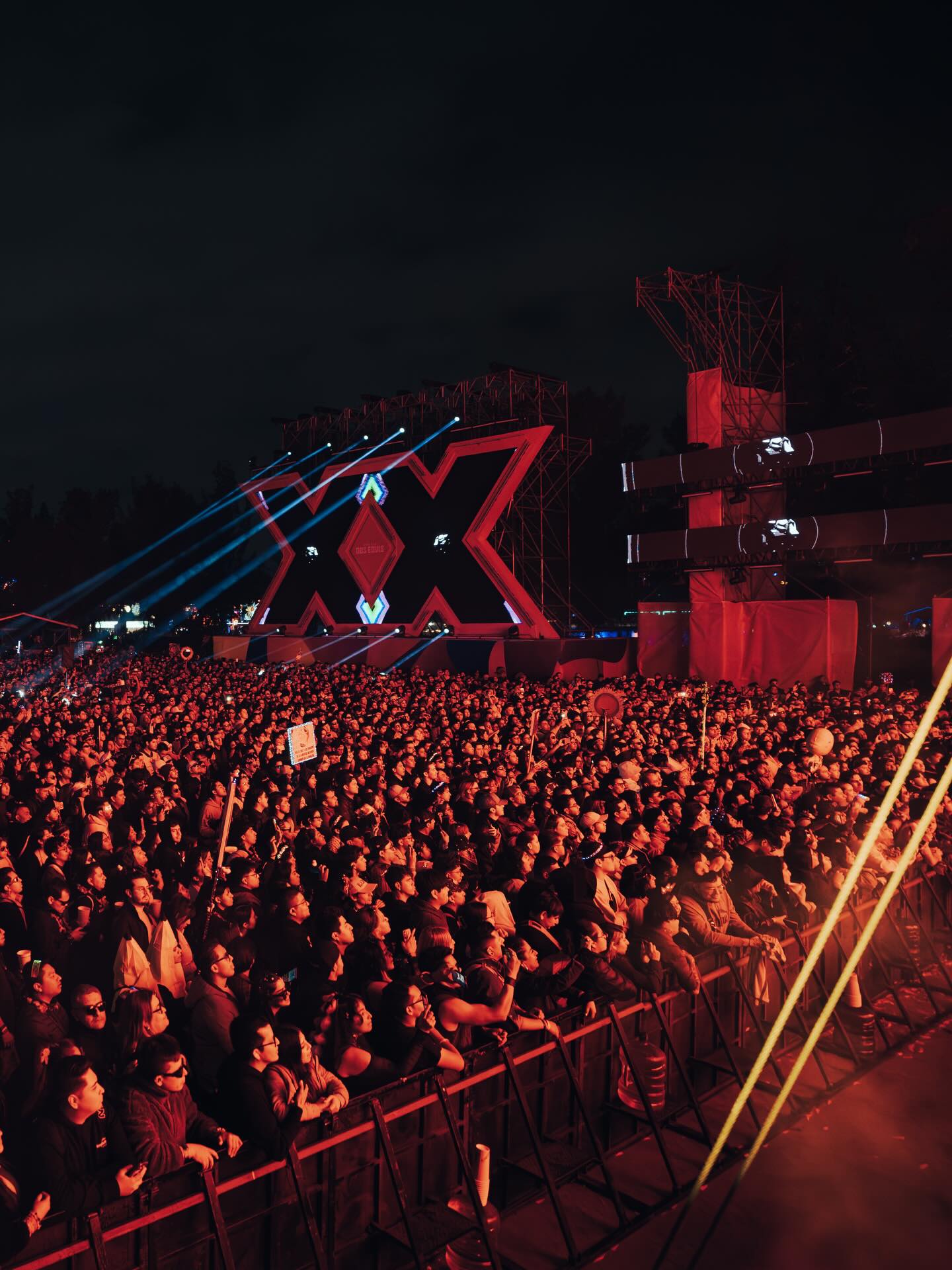 Built Dos Equis stage at EDC México 2026 photographed from the crowd, with beam lighting and the illuminated XX structure.
