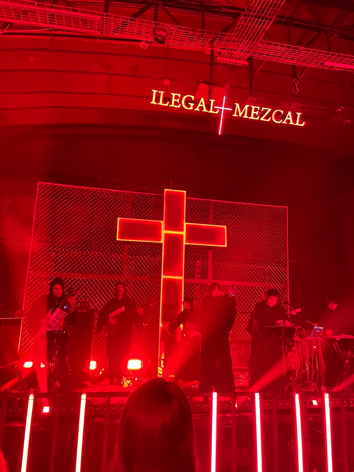 Fiesta Ilegal stage adapted and built in the final venue, with performers, red illumination, metal mesh and the illuminated cross.